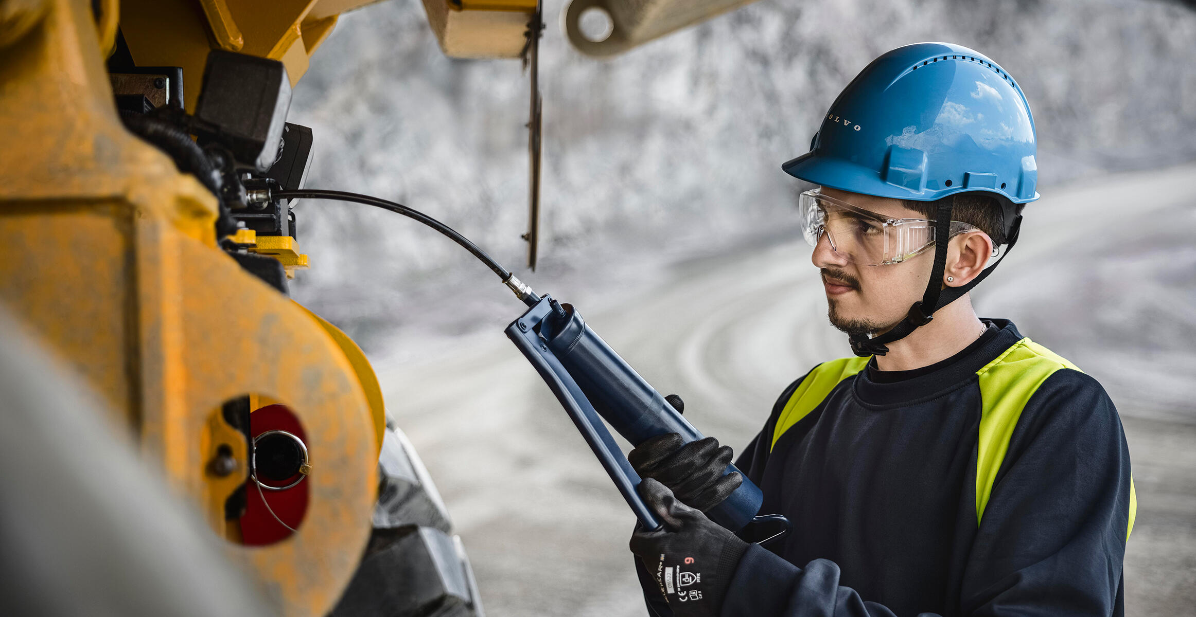 A technician is lubricating a Volvo Articulated Hauler using a greasing gun.
