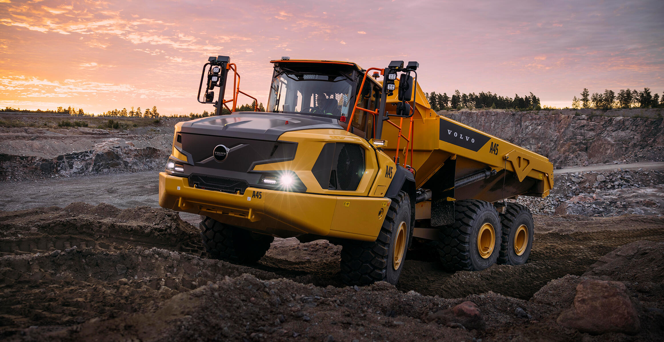A Volvo A45 Articulated Hauler is driving over adverse terrain in a quarry as the sun sets.