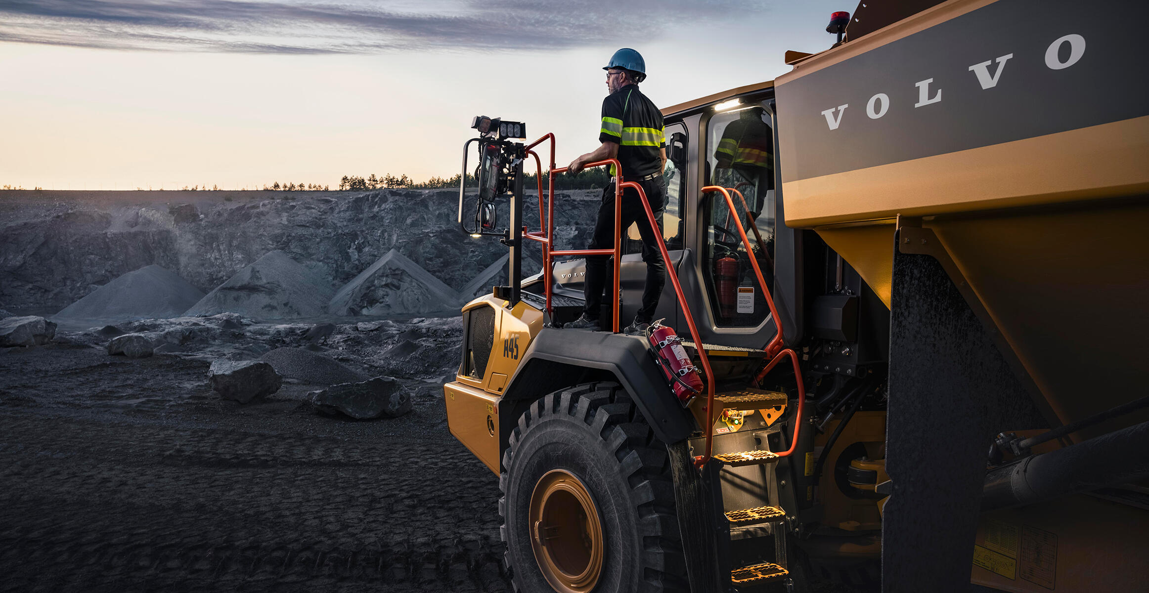 An operator stands on the platform of an A45 Volvo Articulated Hauler looking out to a quarry.