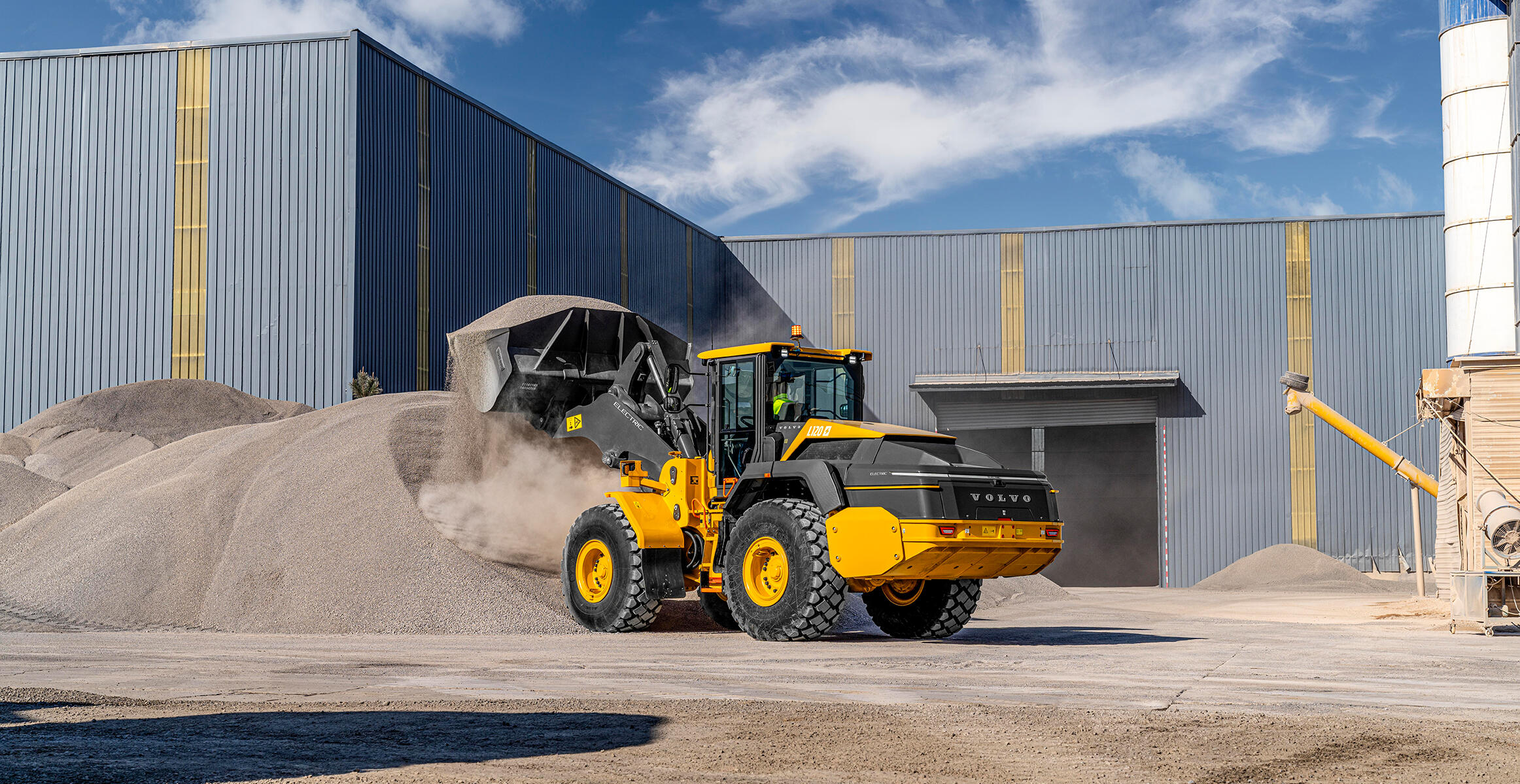 A  Volvo L120H Electric Wheel Loader in motion, lifting materials with its front-mounted bucket in a construction site.