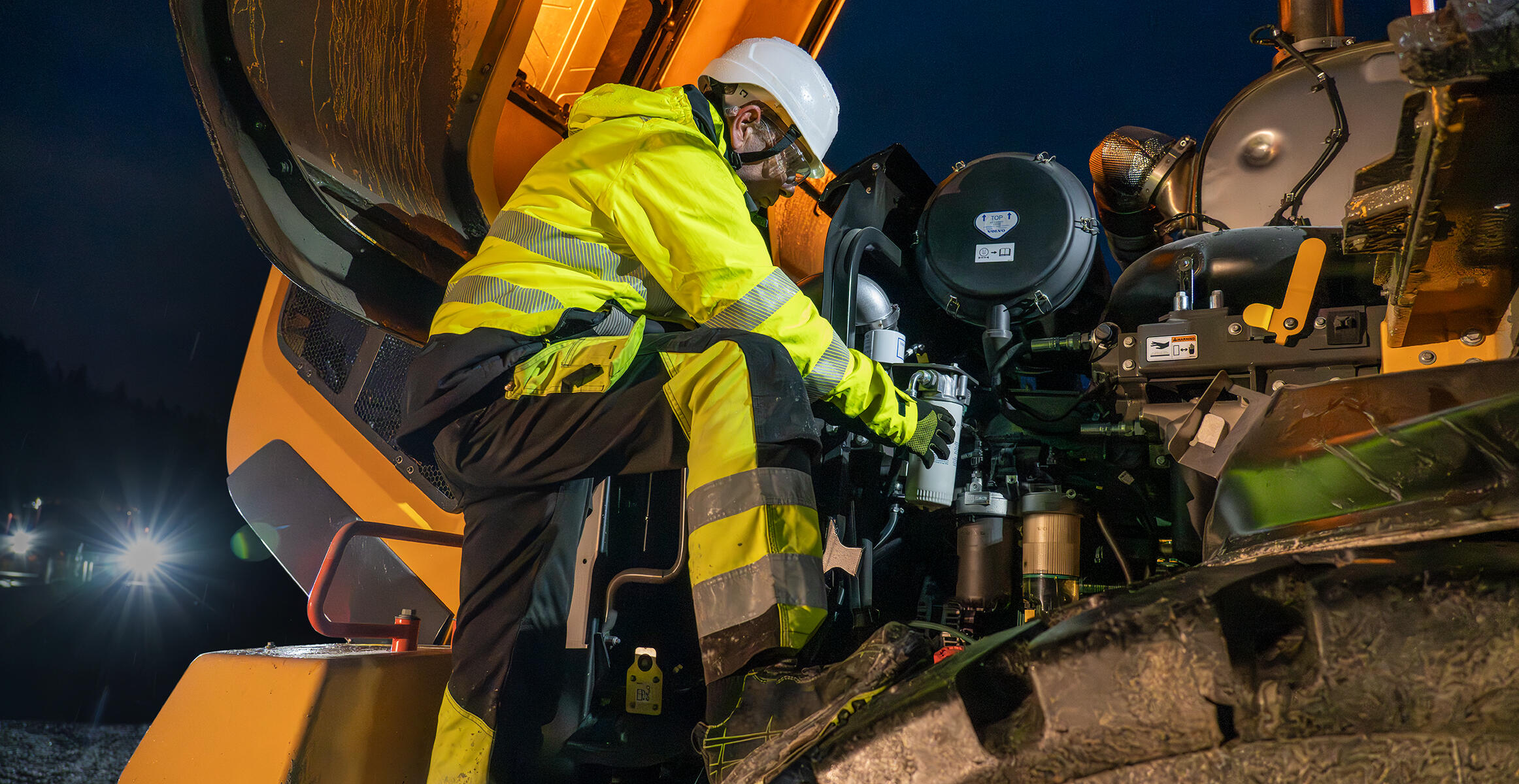 Volvo wheel loader being serviced by technician at night