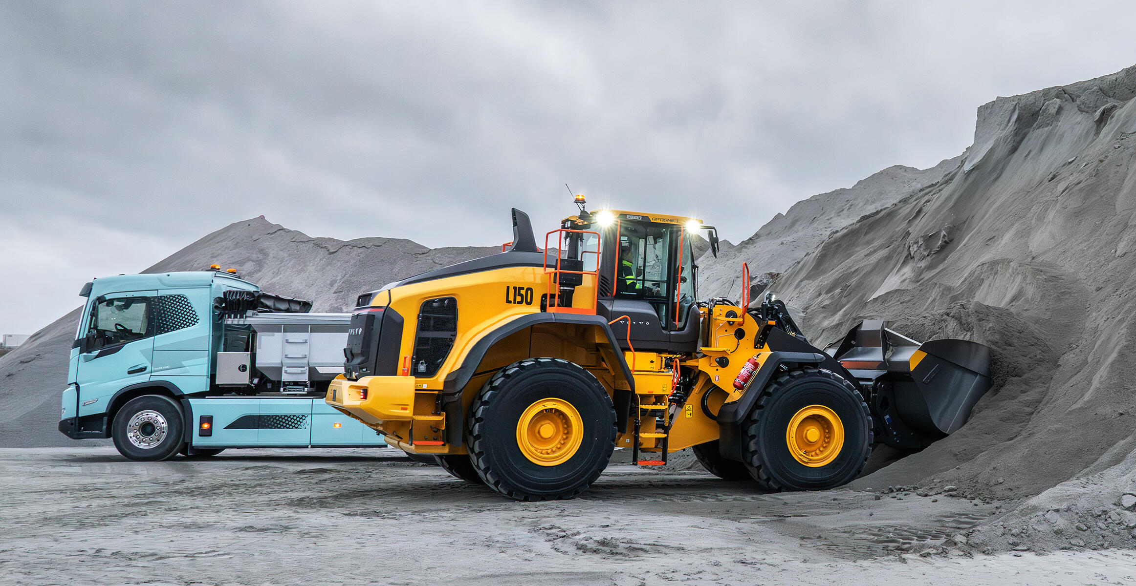 Volvo L150 wheel loader loading from pile in quarry environment with a Volvo truck working in the background