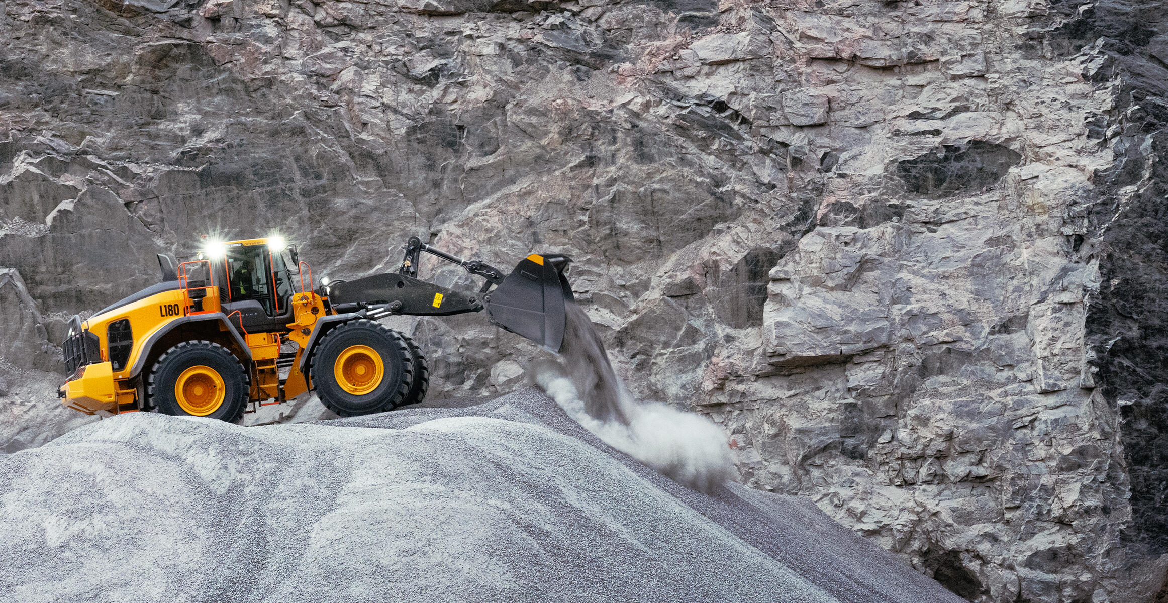 Volvo L180 wheel loader travelling across quarry at speed with full bucket